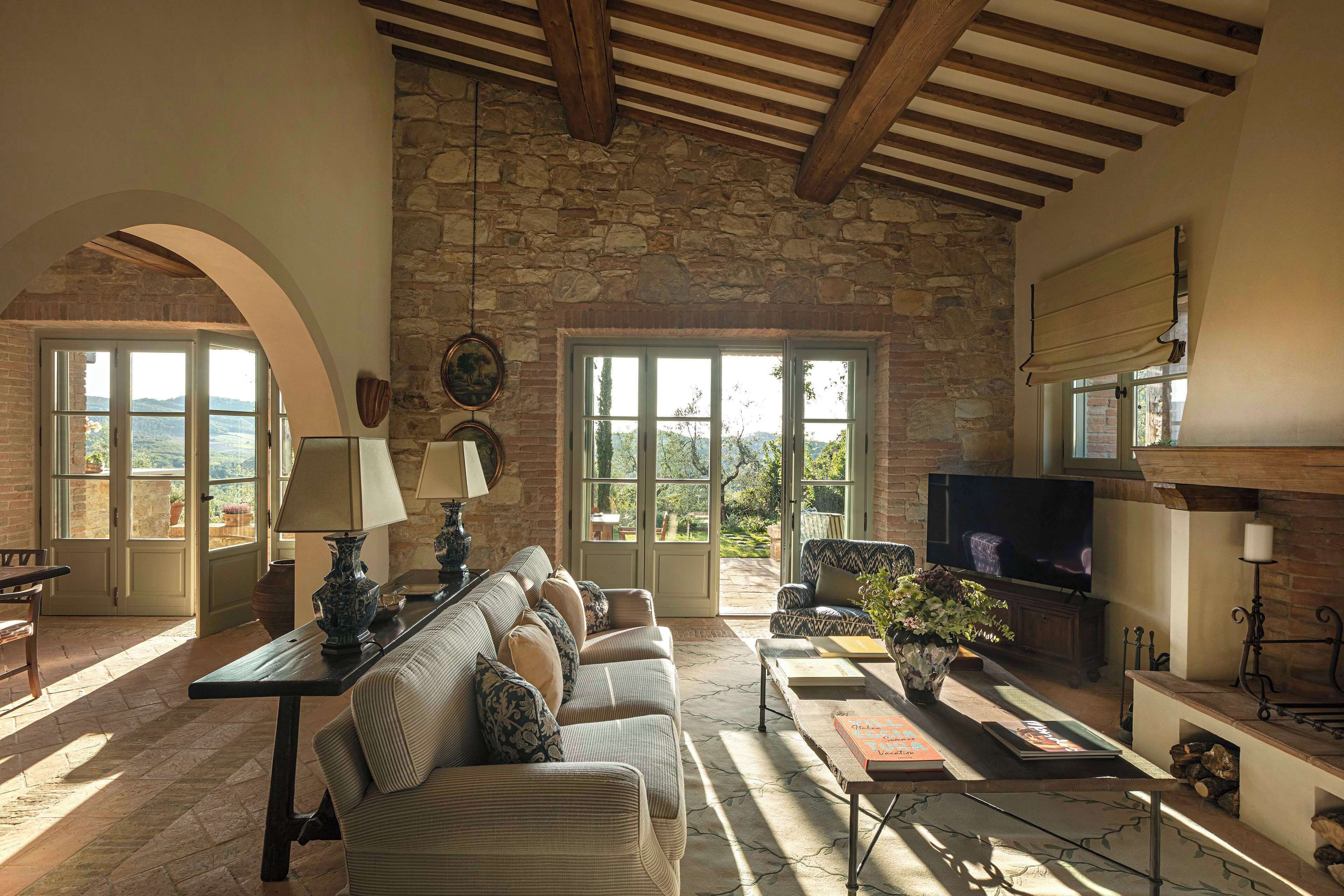 Amplia sala de estar con pared de piedra, televisor grande, chimenea y vista al exterior.
