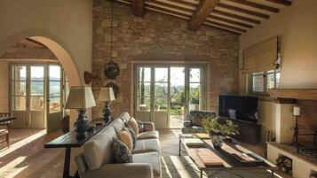 Amplia sala de estar con pared de piedra, televisor grande, chimenea y vista al exterior.