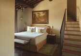 A bedroom with a bed, bedside tables, a painting, a staircase, and a bench.