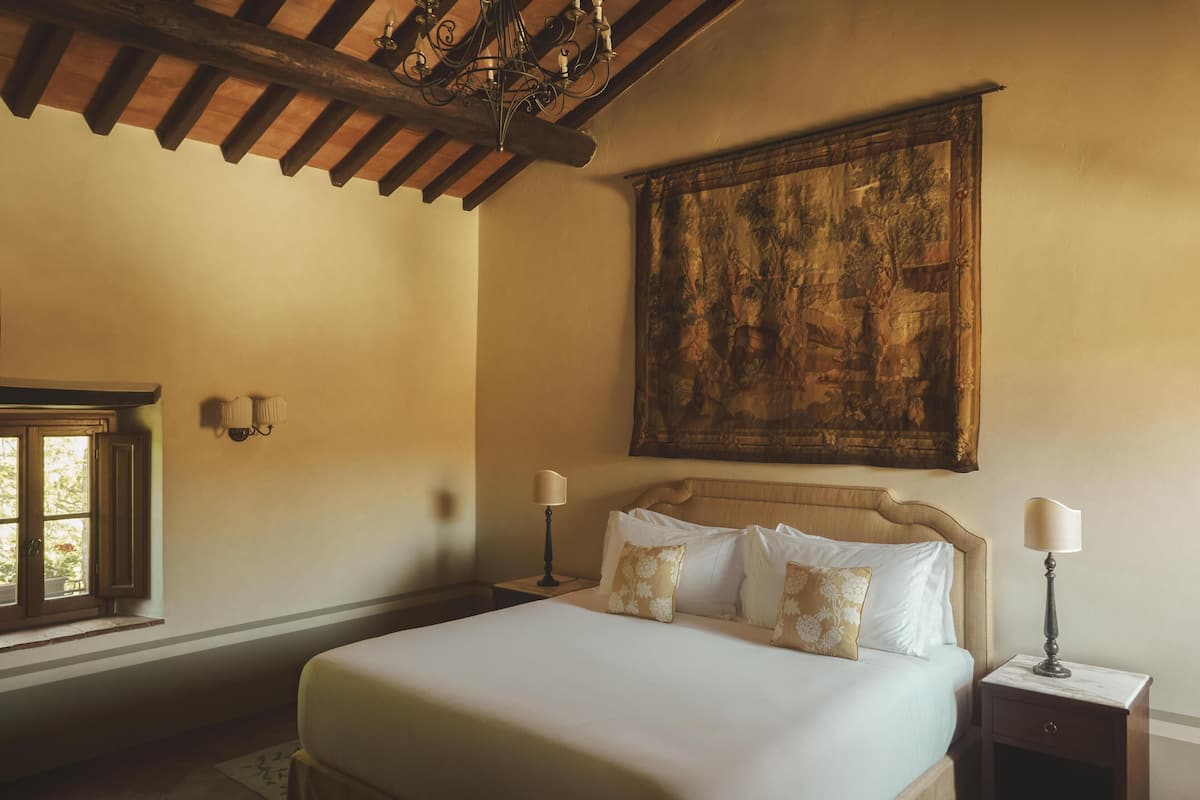 A bedroom with a large bed, a wooden ceiling, a painting on the wall, and a window with curtains.