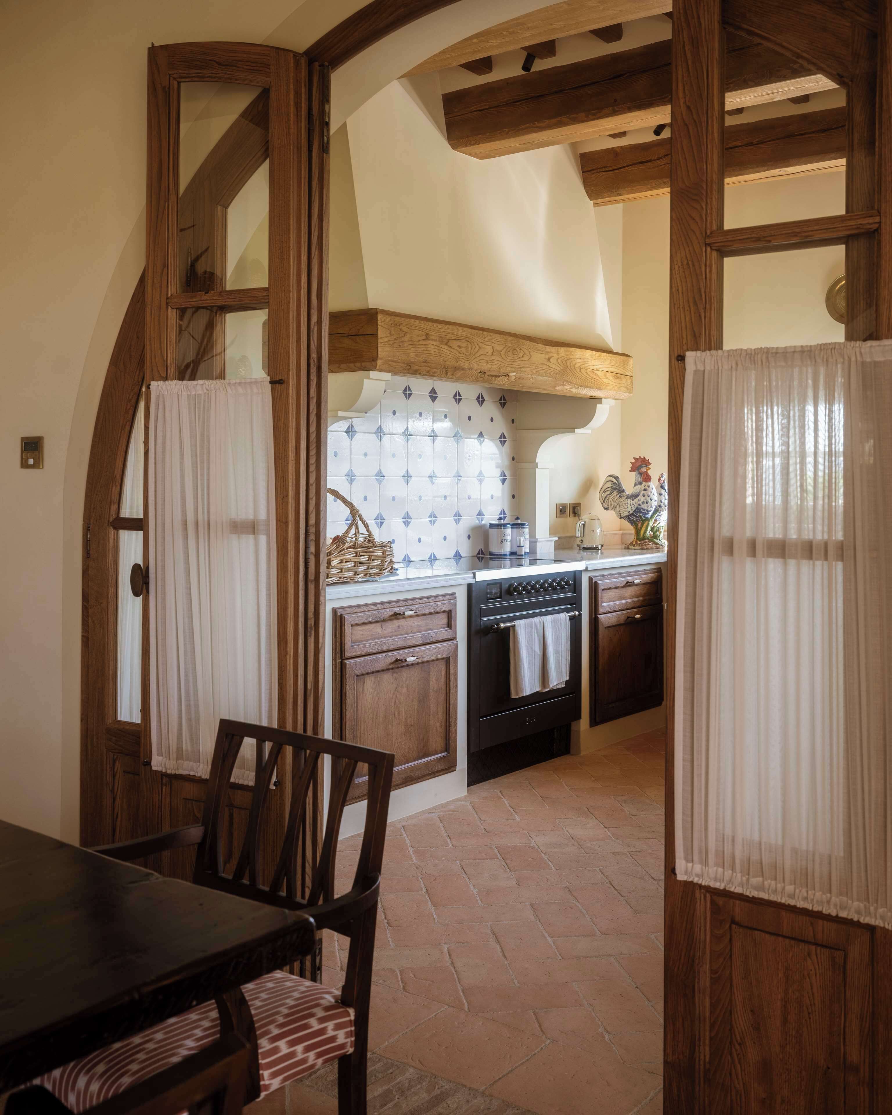 A rustic kitchen with wooden beams, a tiled backsplash, and a dining area with a table and chairs.