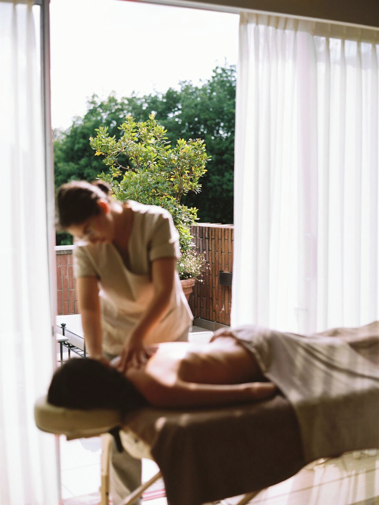 A person receiving a massage in a room with a view of trees and a wooden fence.