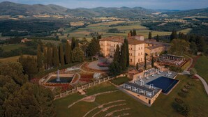 Vista aerea di una vasta proprietà con un edificio centrale circondato da giardini curati, una piscina e una fontana.