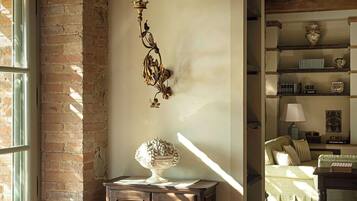 A room with a stone wall, wooden beams, a cabinet with a lamp, and a bed with a green bedspread.