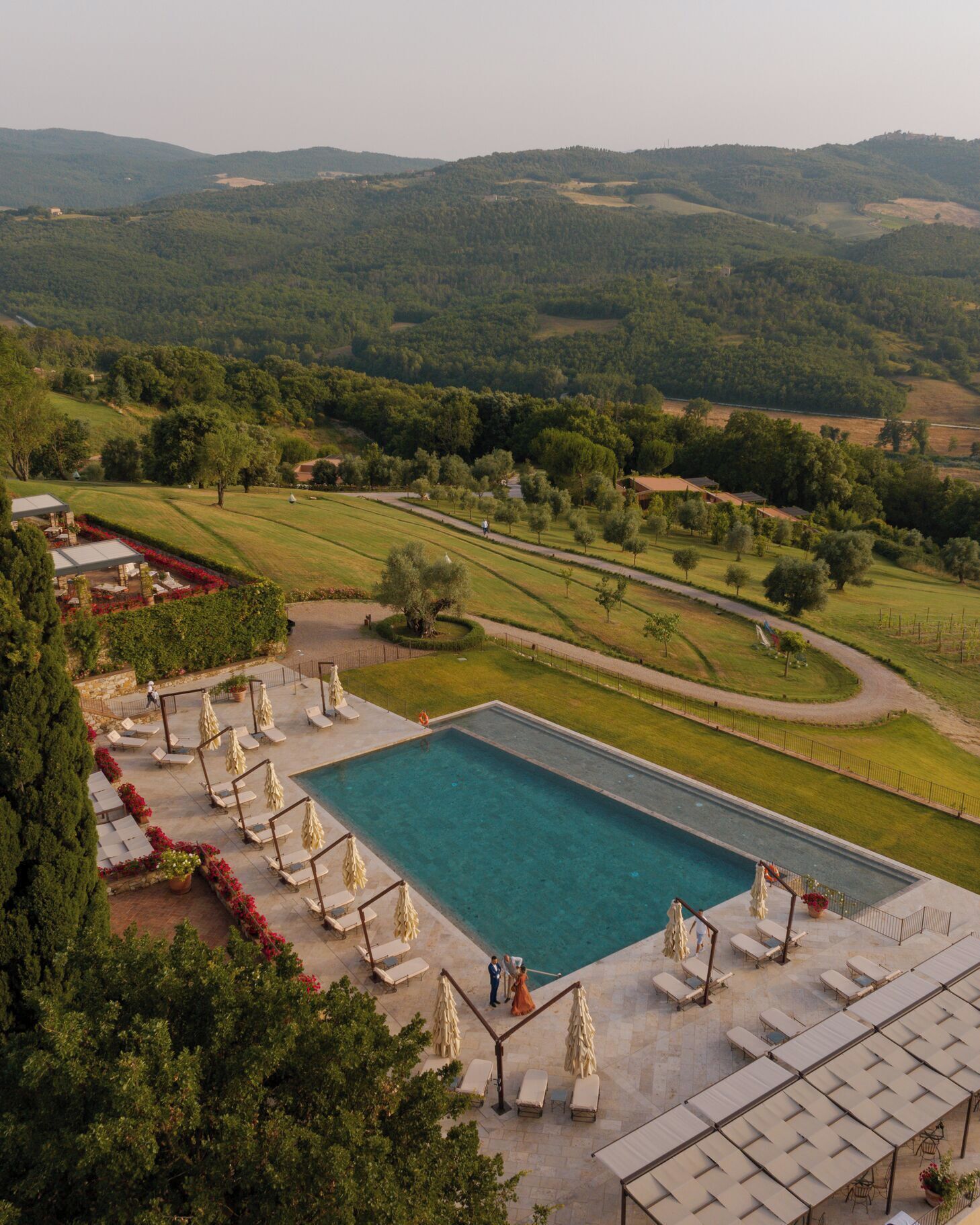 Un espace piscine agrémenté de chaises longues et de parasols, entouré d’un jardin aménagé et offrant une vue sur des collines verdoyantes.