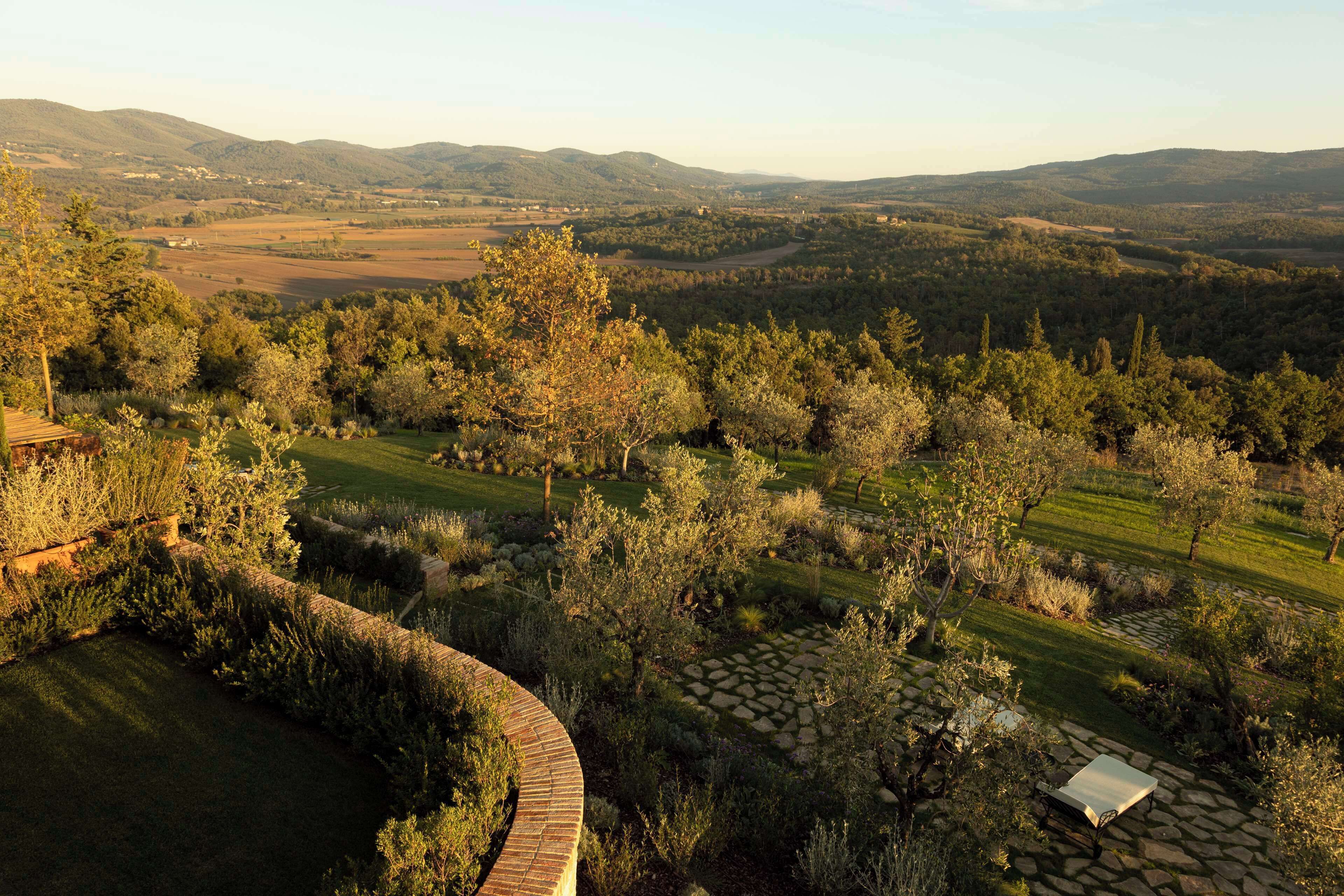 Un giardino curato con un vialetto in pietra, una piccola costruzione bianca e vista su colline lontane.
