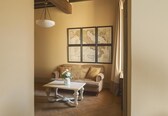 A room with a wooden ceiling, a white table with a vase, a beige sofa, and framed maps on the wall.