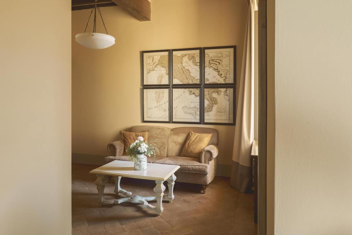 A room with a wooden ceiling, a white table with a vase, a beige sofa, and framed maps on the wall.