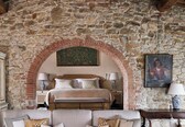 A bedroom with a stone wall, a bed with a headboard, two bedside tables with lamps, a cabinet, and a painting.