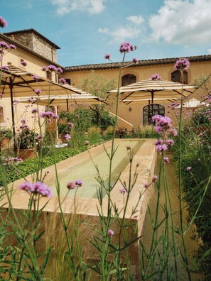 A courtyard with a pool, outdoor seating, and a building with a tiled roof.