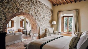 Una camera da letto con un arco in pietra, un letto, una sedia, un tavolo e una finestra con tende.
