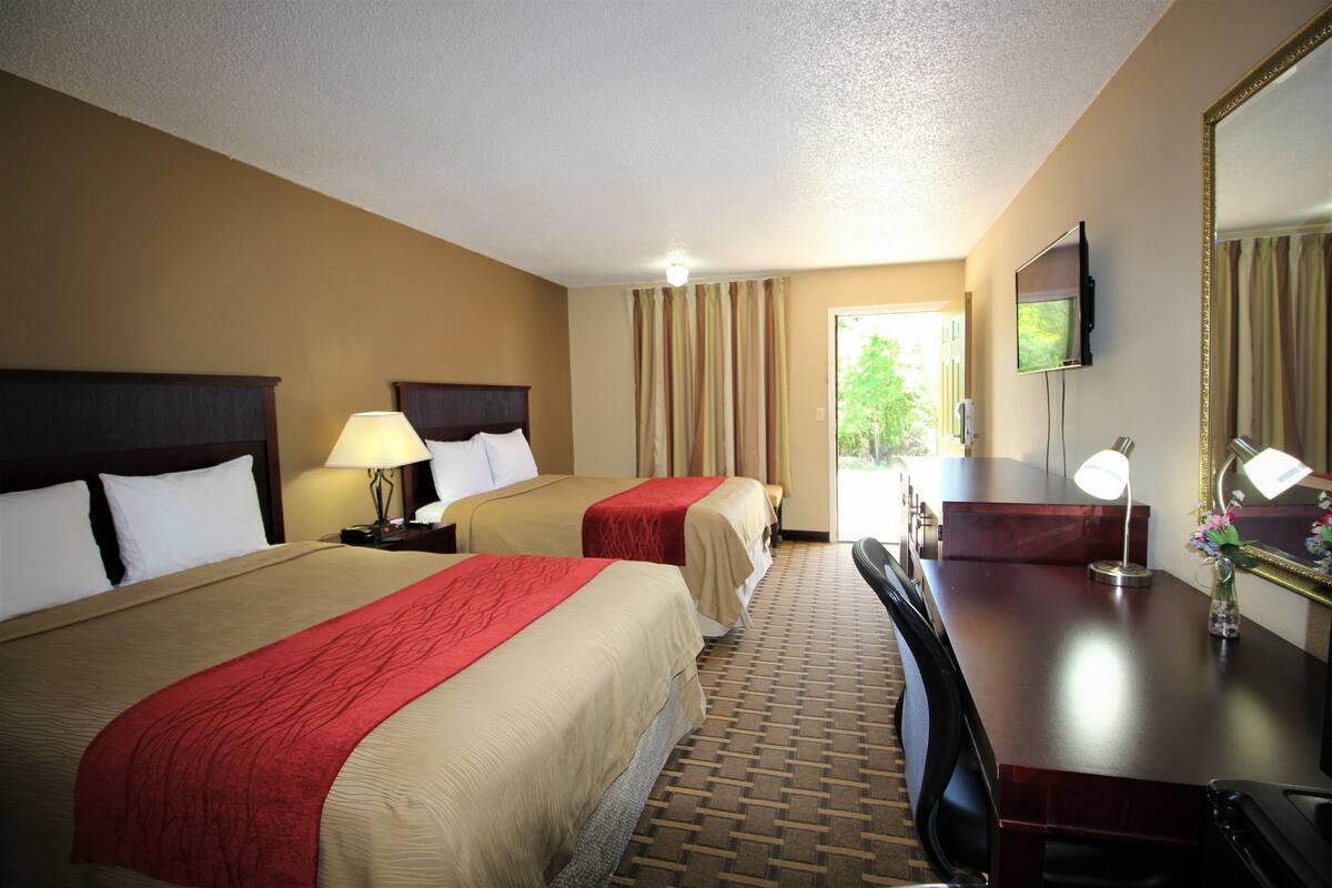 A hotel room with two beds, a desk, a chair, a TV, and a window with curtains.