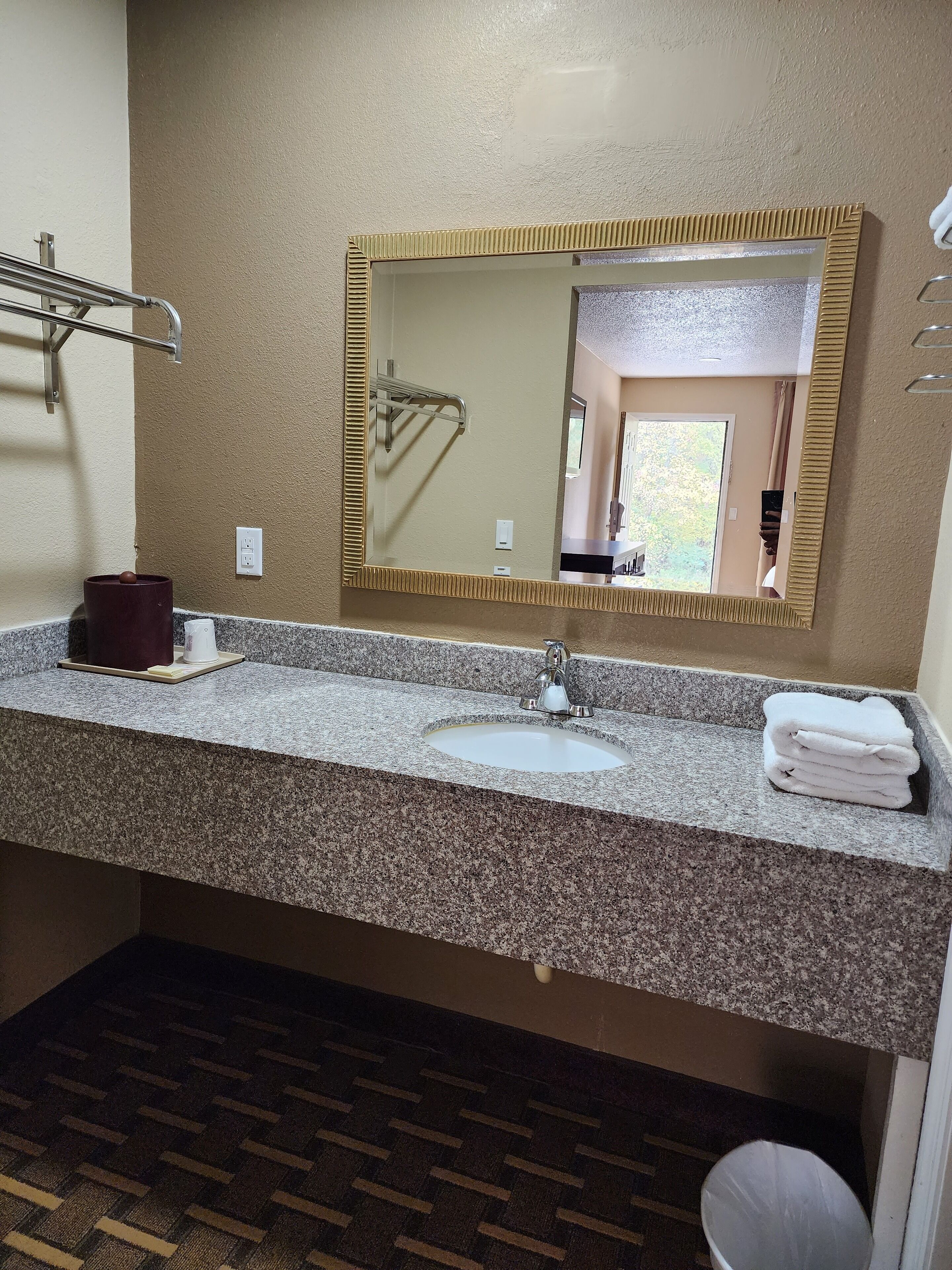 A bathroom with a granite countertop, a sink, a mirror, and a towel rack.