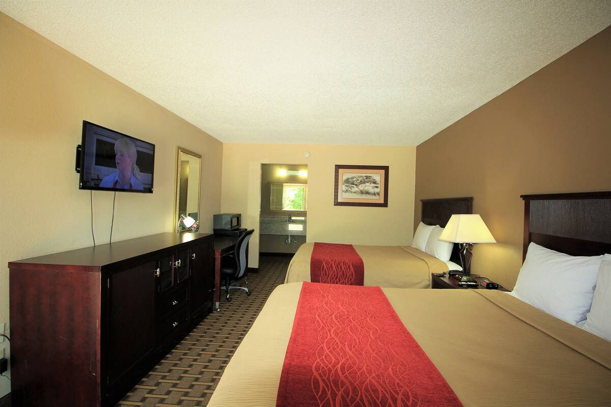 A hotel room with two beds, a TV, a desk, and a mirror.