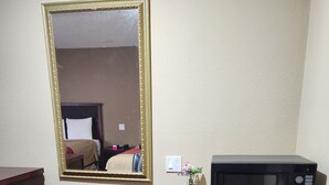 Ein Hotelzimmer mit einem Holztisch, einem schwarzen Bürostuhl, einem schwarzen Kühlschrank und einem großen Spiegel an der Wand.