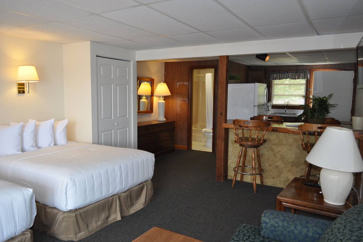 A hotel room with a bed, a desk with a chair, a small kitchen area, and a bathroom.