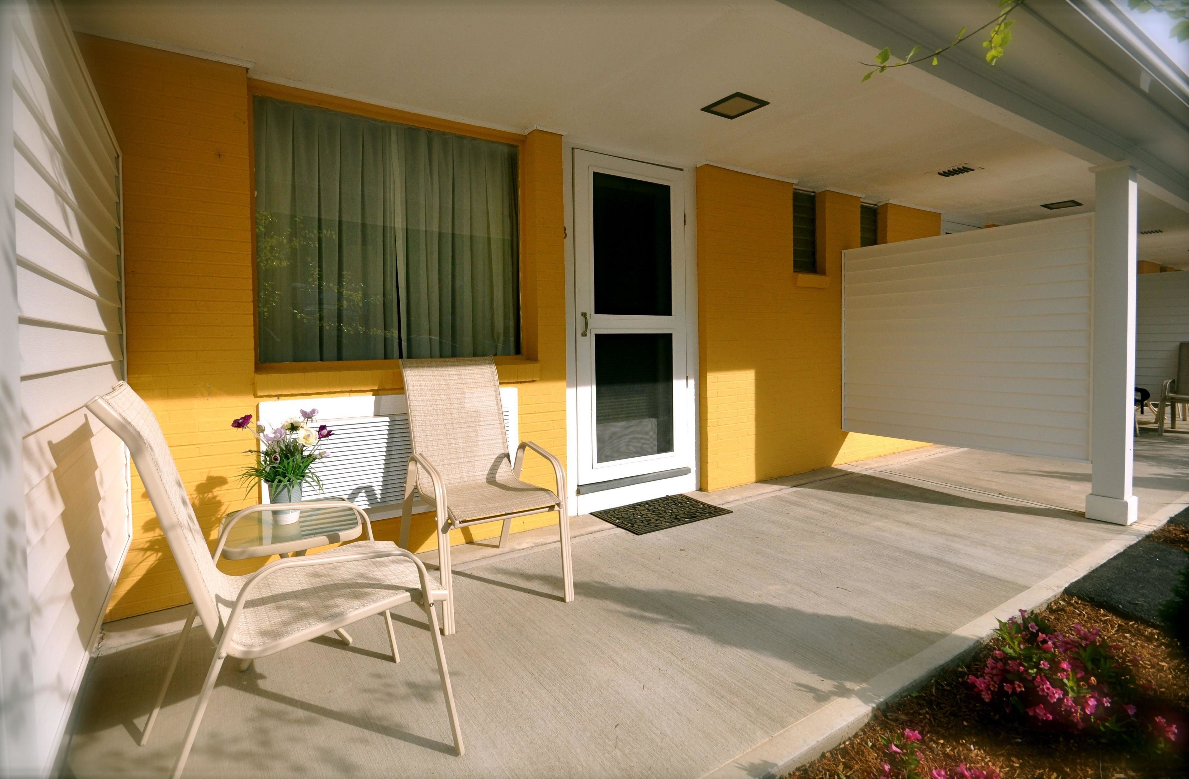 A covered porch with two chairs, a small table, and a potted plant.