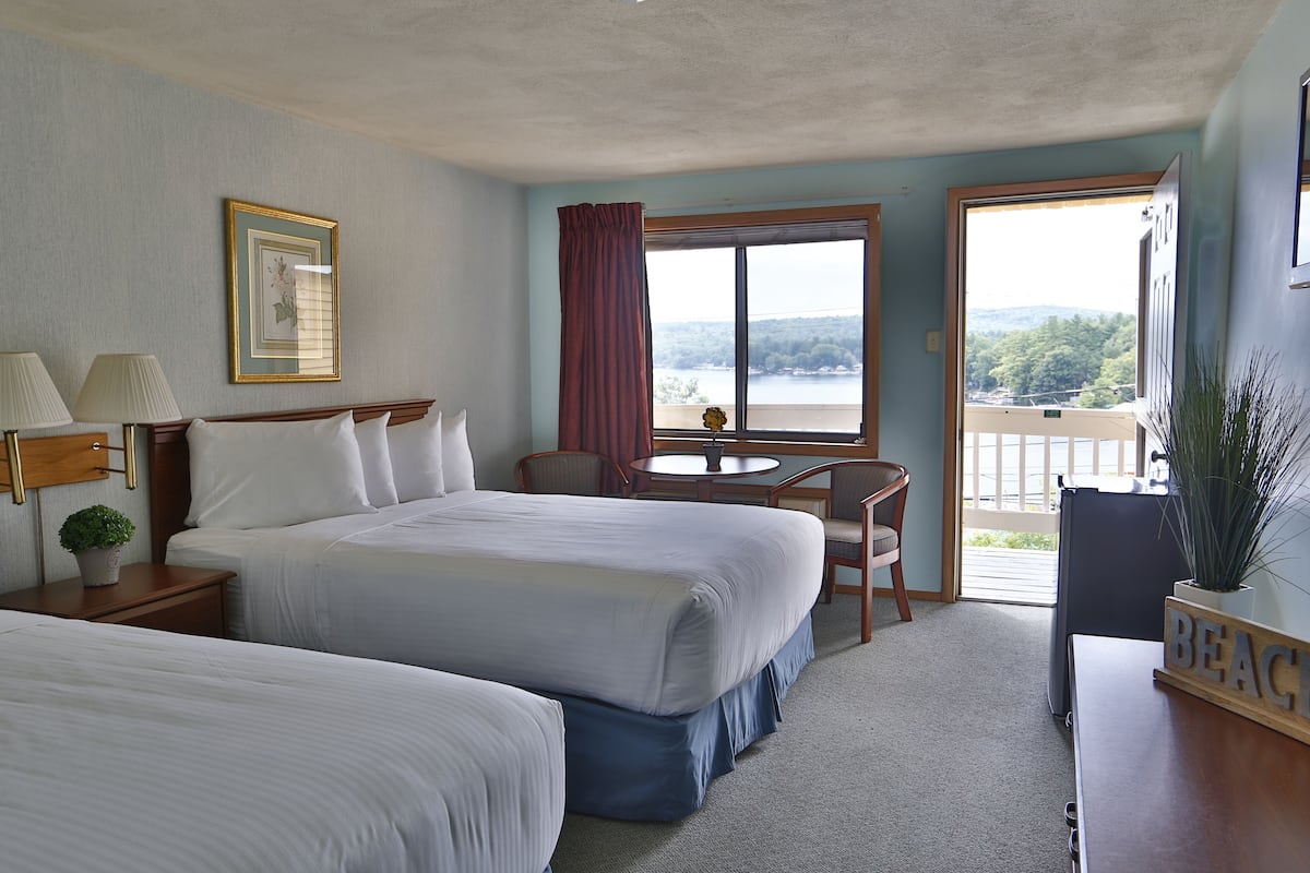 A hotel room with two beds, a desk, a chair, a window with a view, and a balcony.