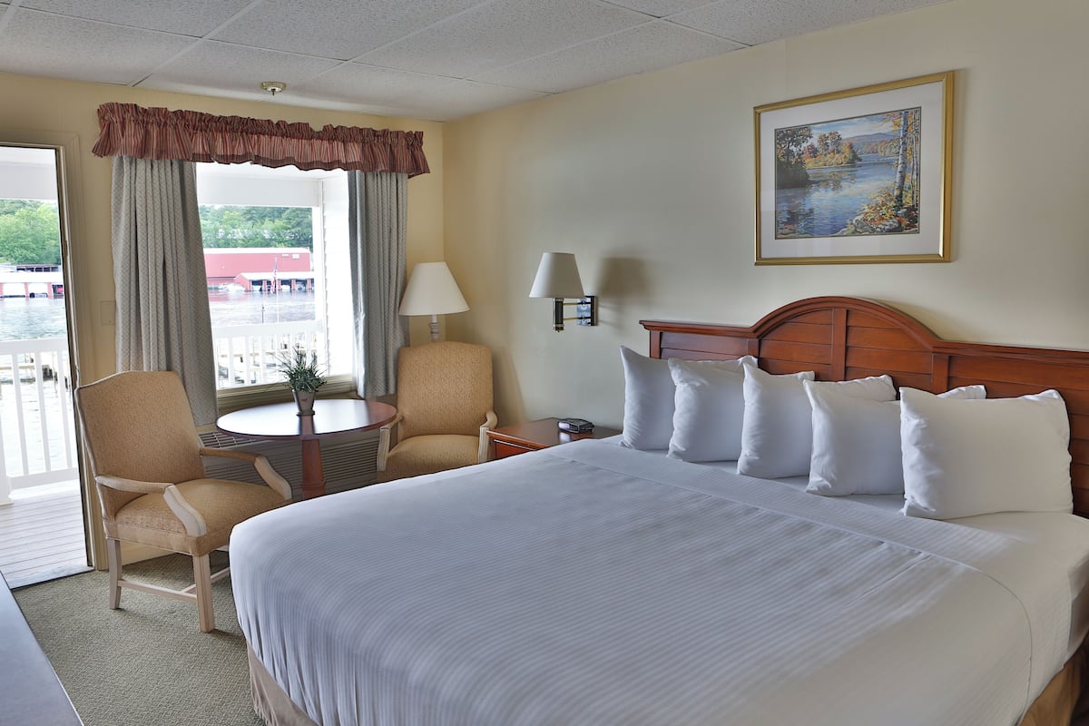 A hotel room with a large bed, two chairs, a small table, a lamp, and a painting on the wall.