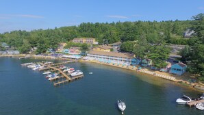 A coastal area with a marina, docked boats, and a row of beachside buildings with umbrellas. - The Naswa Resort (Laconia)