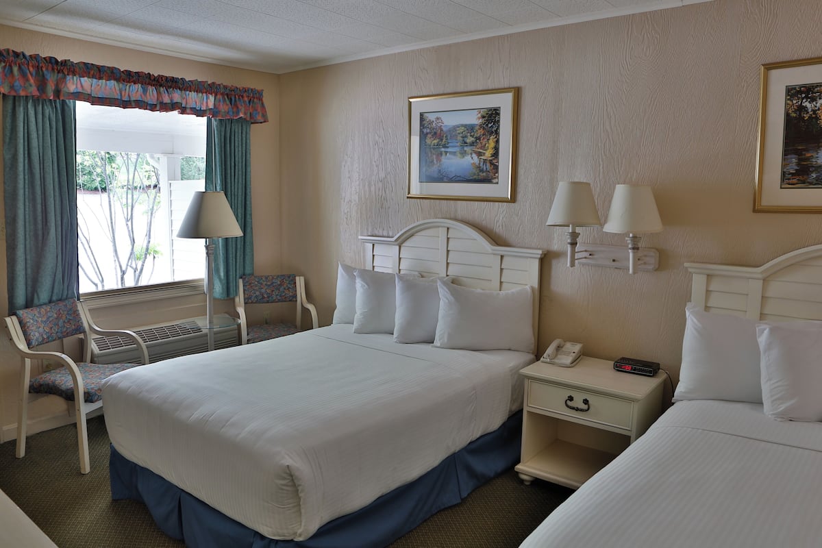 A hotel room with a large bed, two bedside tables with lamps, a chair, and a window with curtains.