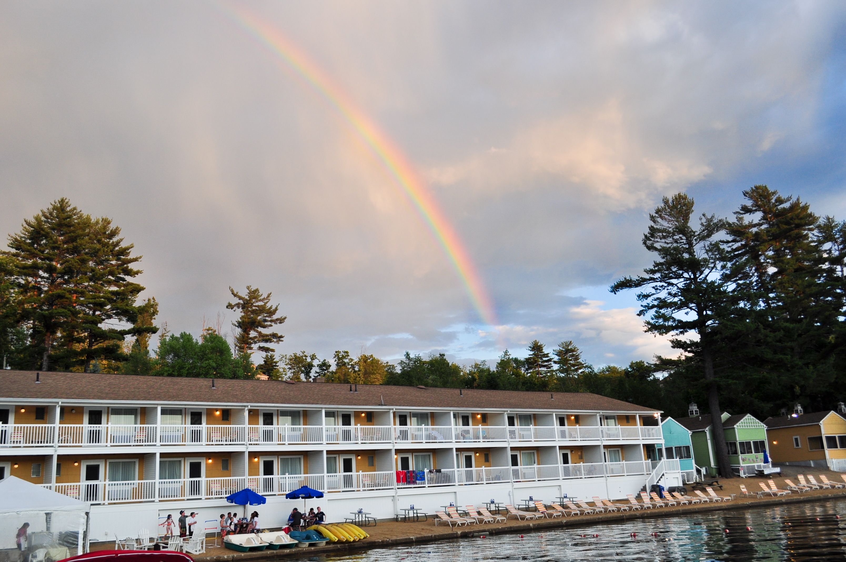Un motel con zona de piscina, un arcoíris y un lago.