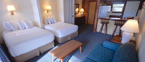 A hotel room with two beds, a sofa, a small table, and a kitchenette.