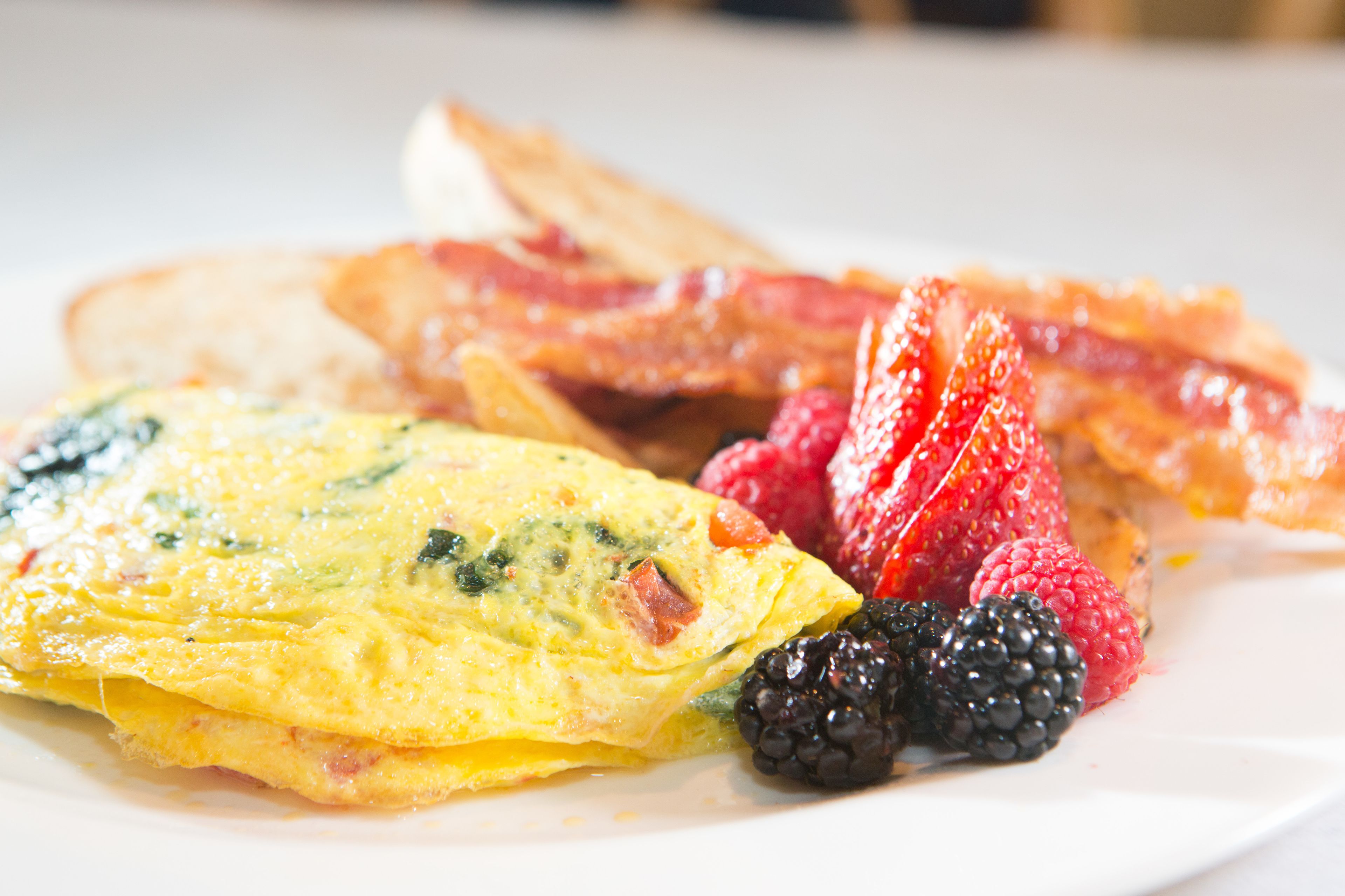 Un plato de desayuno con tortilla, tocino, fresas y moras.