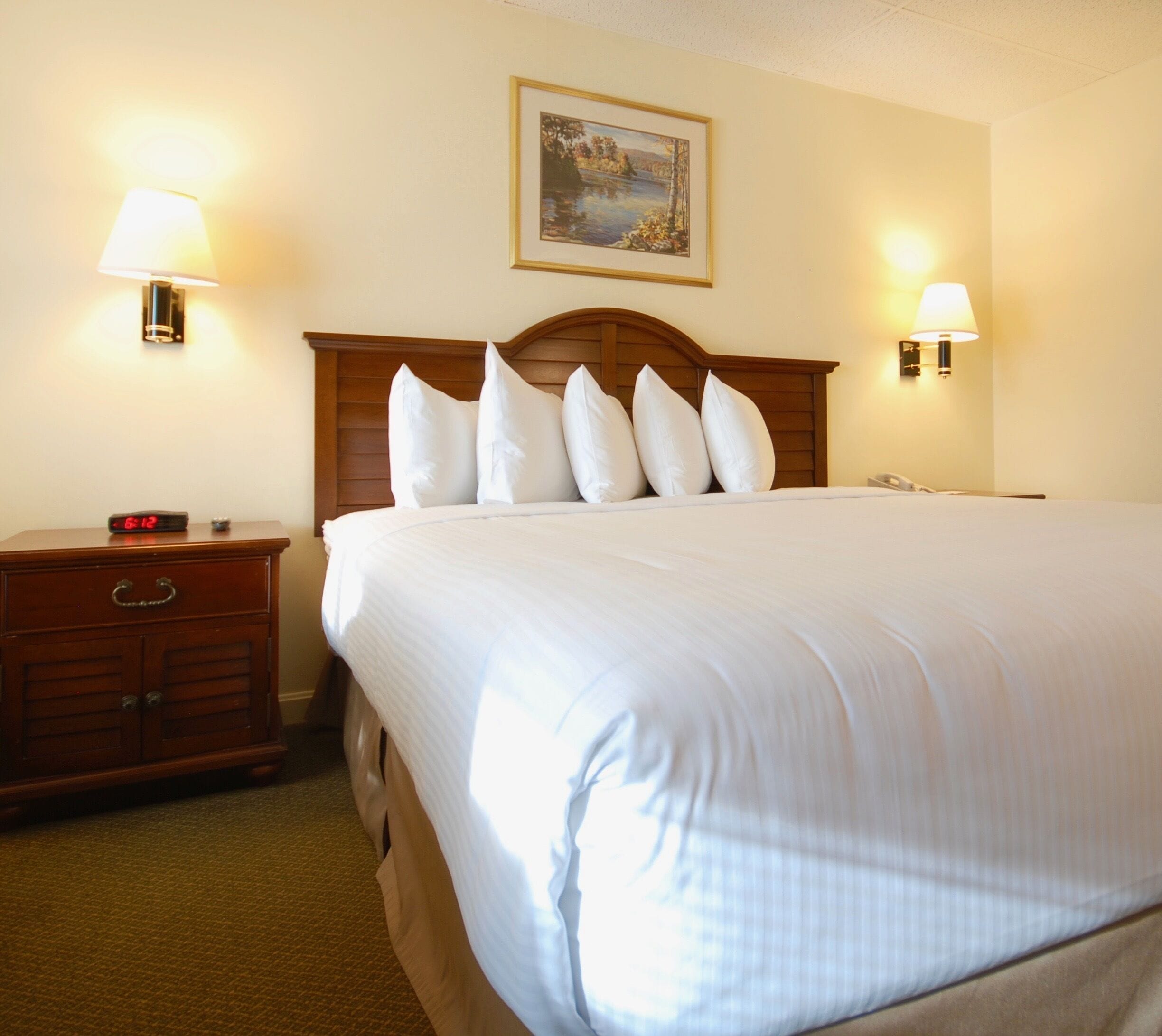 A hotel room with a large bed, wooden headboard, and two bedside lamps.