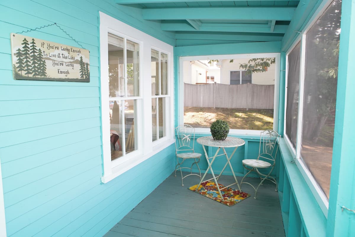 A turquoise porch with a small table and two chairs, a decorative sign, and a view of a backyard.