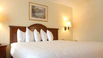 A hotel room with a large bed, wooden headboard, two wall-mounted lamps, a bedside table with a clock, and two framed pictures on the walls.