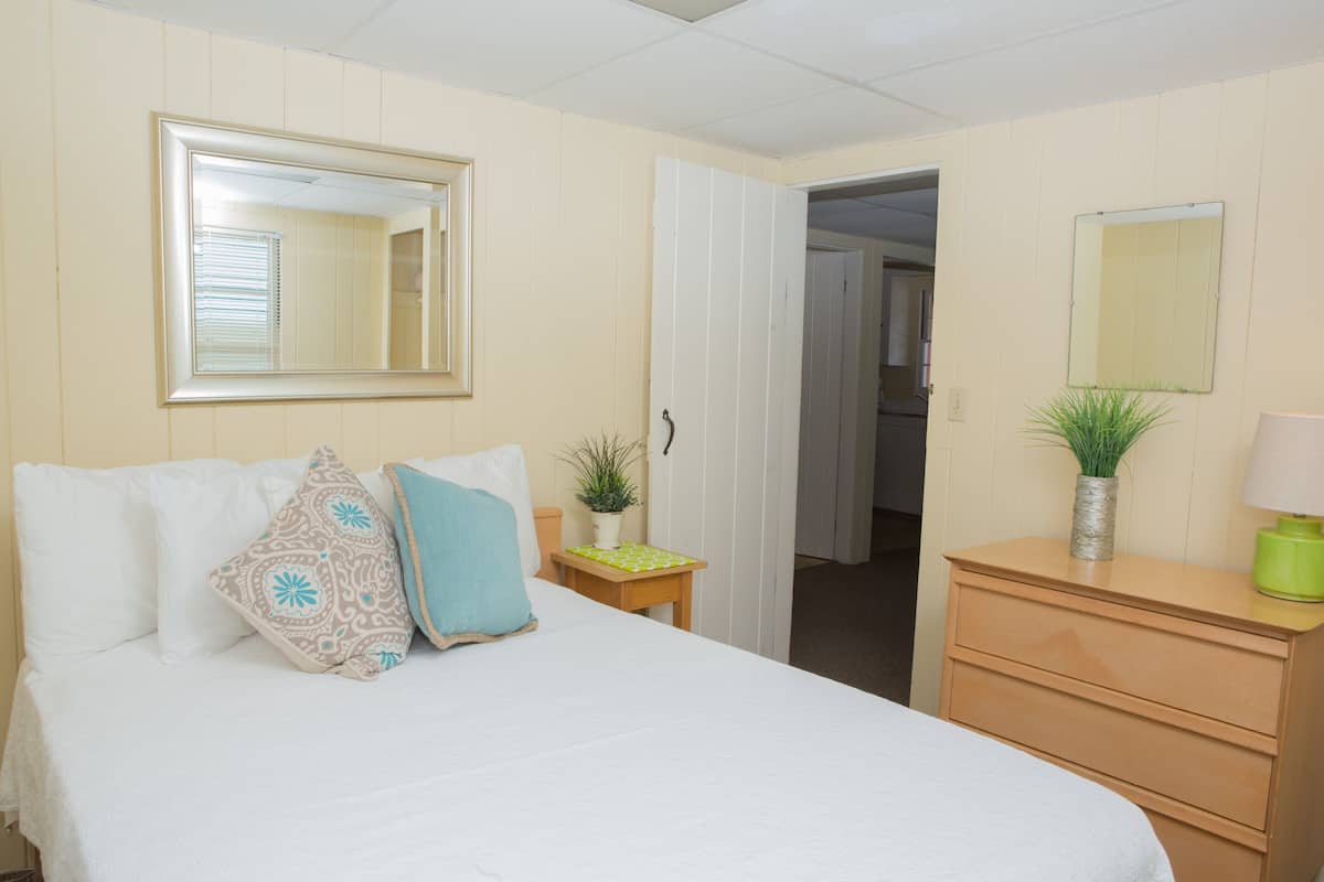 A neatly arranged bedroom with a bed, bedside tables, a dresser, and two mirrors.