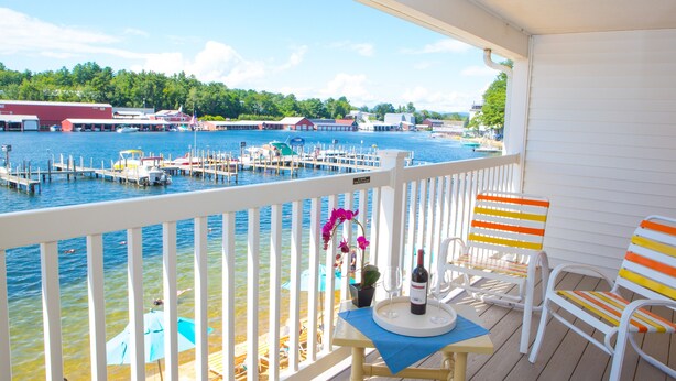 A wooden deck with a table, chairs, and a view of a marina with boats and buildings. - The Naswa Resort (Laconia)