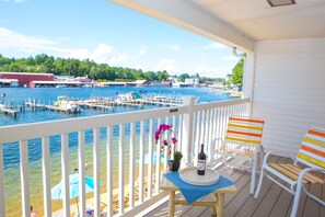 A wooden deck with a table, chairs, and a view of a marina with boats and buildings.