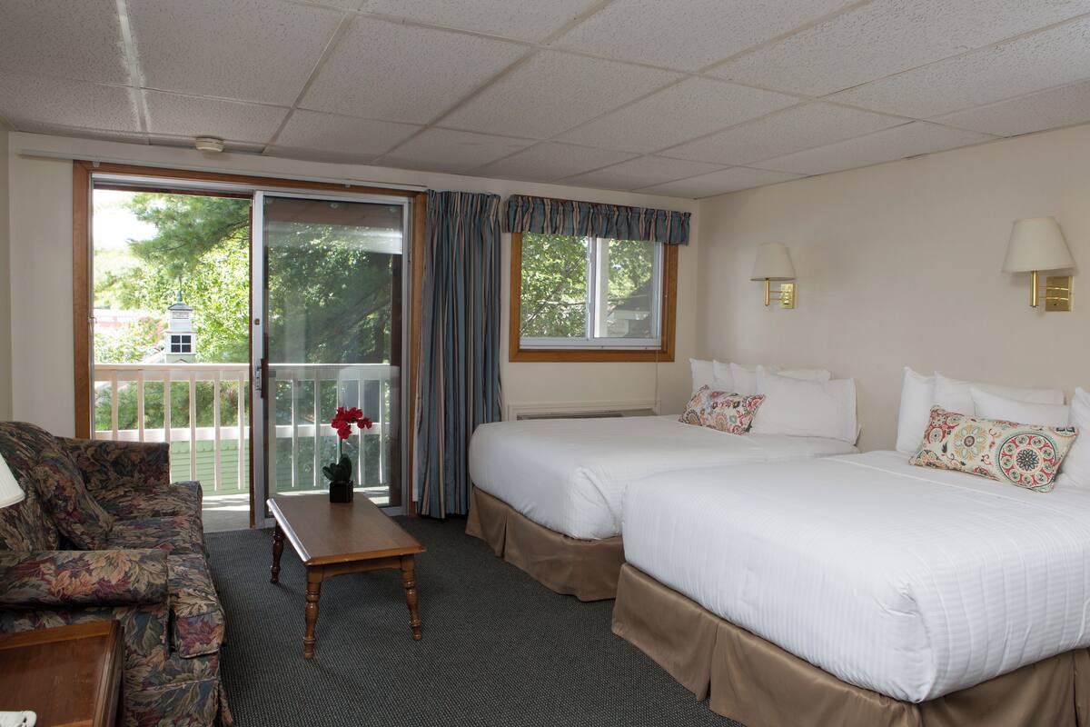 A hotel room with two beds, a sofa, a table, and a view of the outdoors.