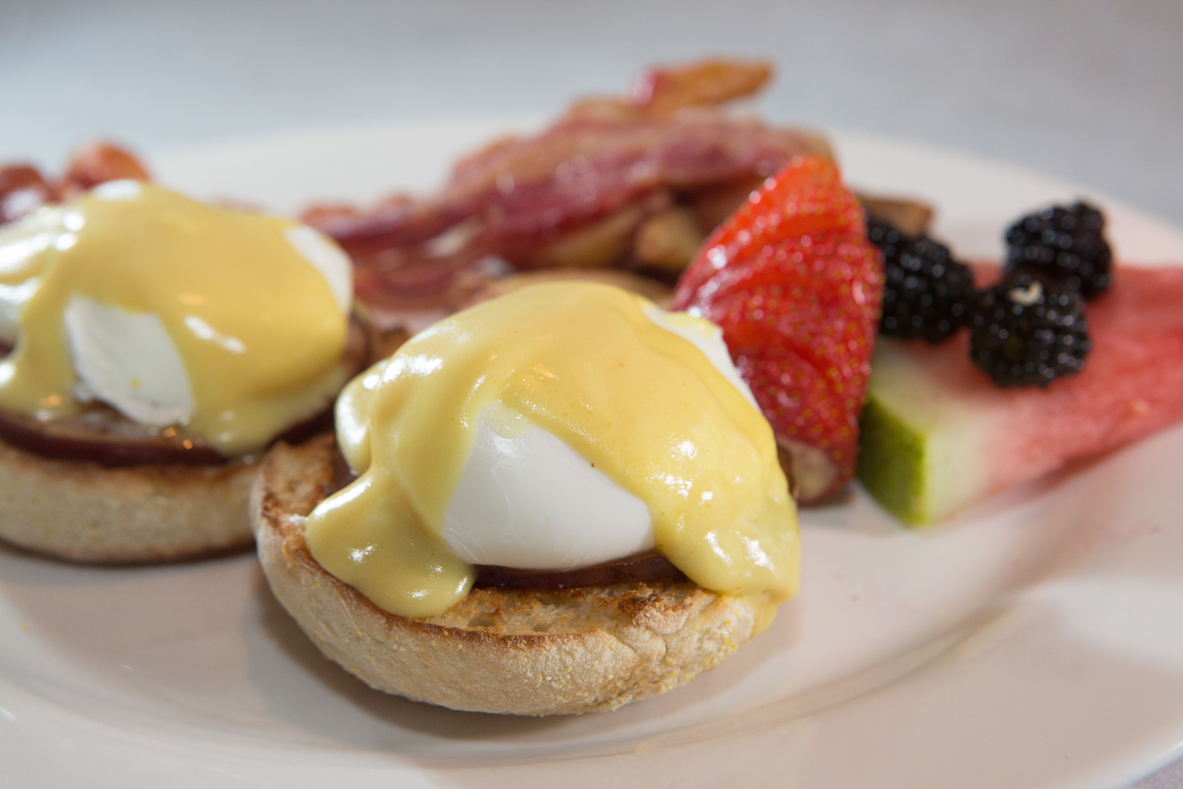 Ein Frühstücksteller mit Eggs Benedict, Speck, Erdbeeren, Brombeeren und einem Melonenstück.
