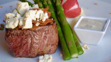 A steak topped with cheese and served with asparagus and a small bowl of sauce.