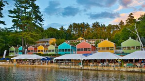 A waterfront hotel with colorful buildings, outdoor seating, and a lake view. - The Naswa Resort (Laconia)
