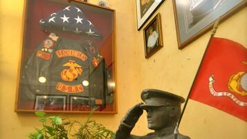 Een standbeeld van een soldaat die zwaait, een ingelijste marinejas van het USMC, en een rode vlag aan een muur.