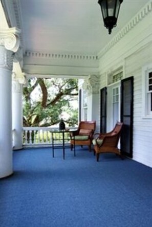 A covered porch with a blue carpet, white columns, and wooden chairs.