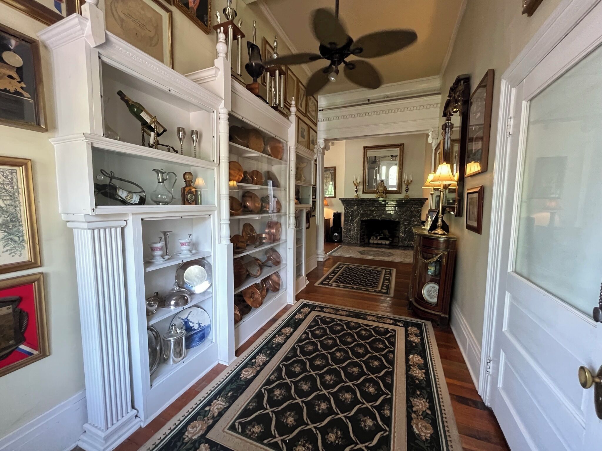 A spacious hallway with white columns, a fireplace, and a ceiling fan.