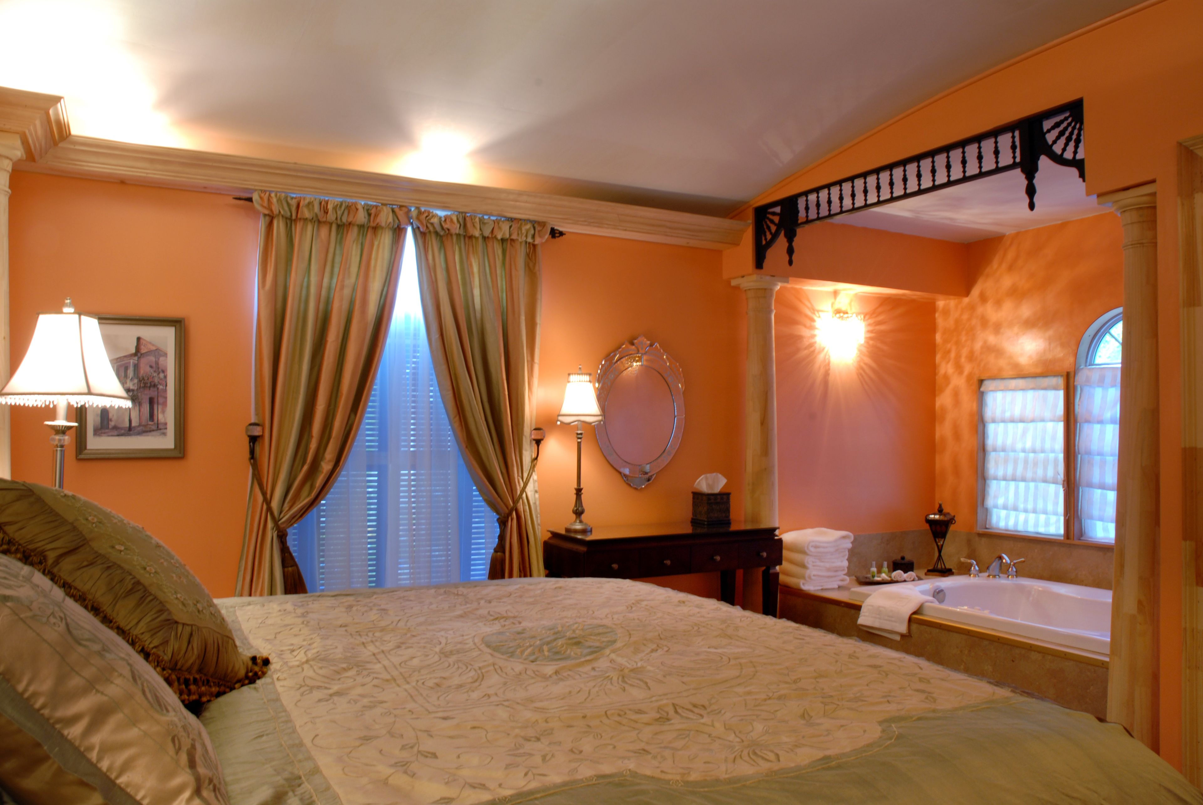 A hotel room with a large bed, a sitting area with a table and chairs, a bathtub, and a window with curtains.