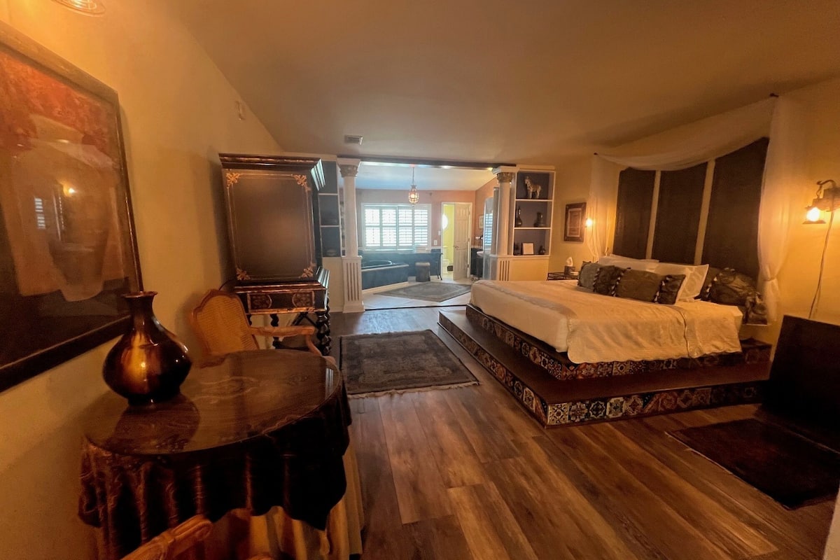 Un dormitorio con una cama grande, un escritorio y una silla. Hay una ventana con cortinas y vistas al exterior.