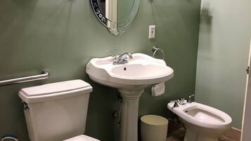 Un baño con inodoro, bidé, lavamanos pedestal y espejo con marco decorativo.