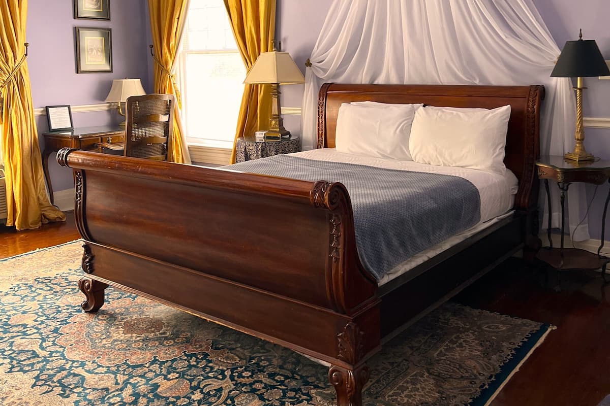 Un dormitorio con una cama con dosel, un dosel, un tapete grande y un ventilador de techo.