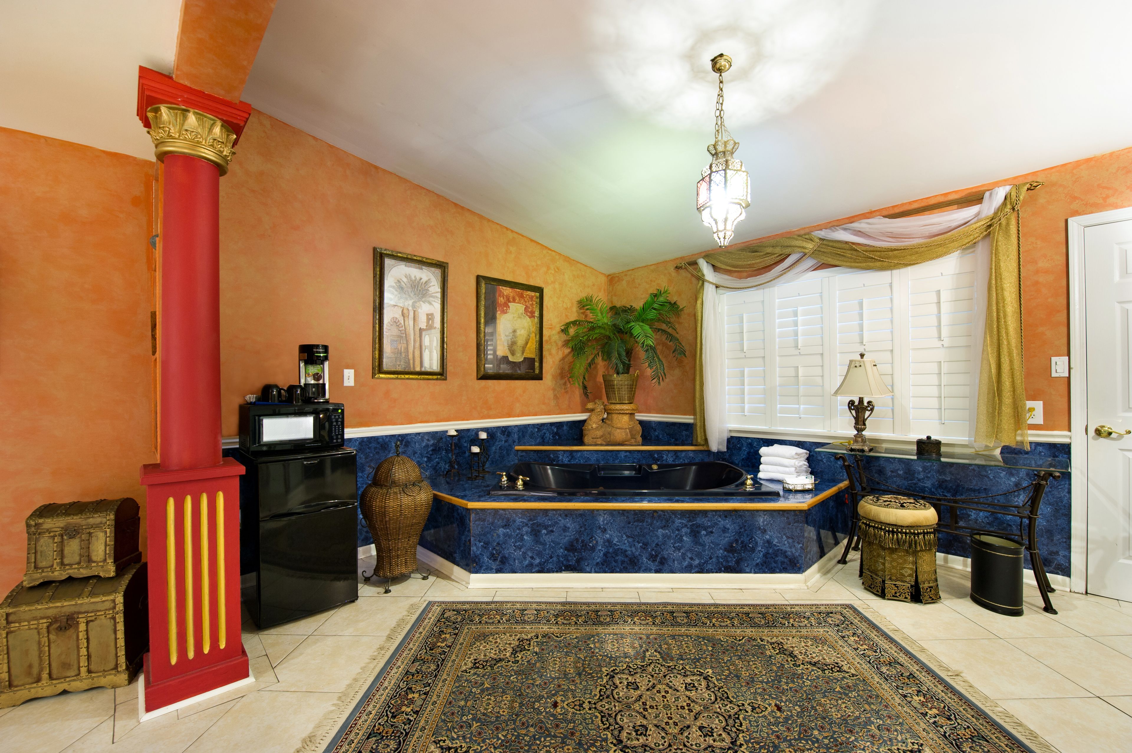 A bathroom with a marble sink, a bathtub, a red column, a potted plant, and a patterned rug.