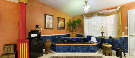 A bathroom with a marble sink, a bathtub, a red column, a potted plant, and a patterned rug.