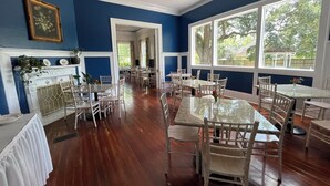 Un espace repas comprenant plusieurs tables et chaises, une cheminée et de grandes fenêtres donnant sur un paysage verdoyant.