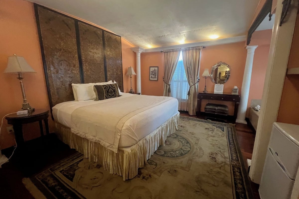 Habitación de hotel con una cama grande, una mesita de noche, un aparador, un espejo y un refrigerador pequeño.