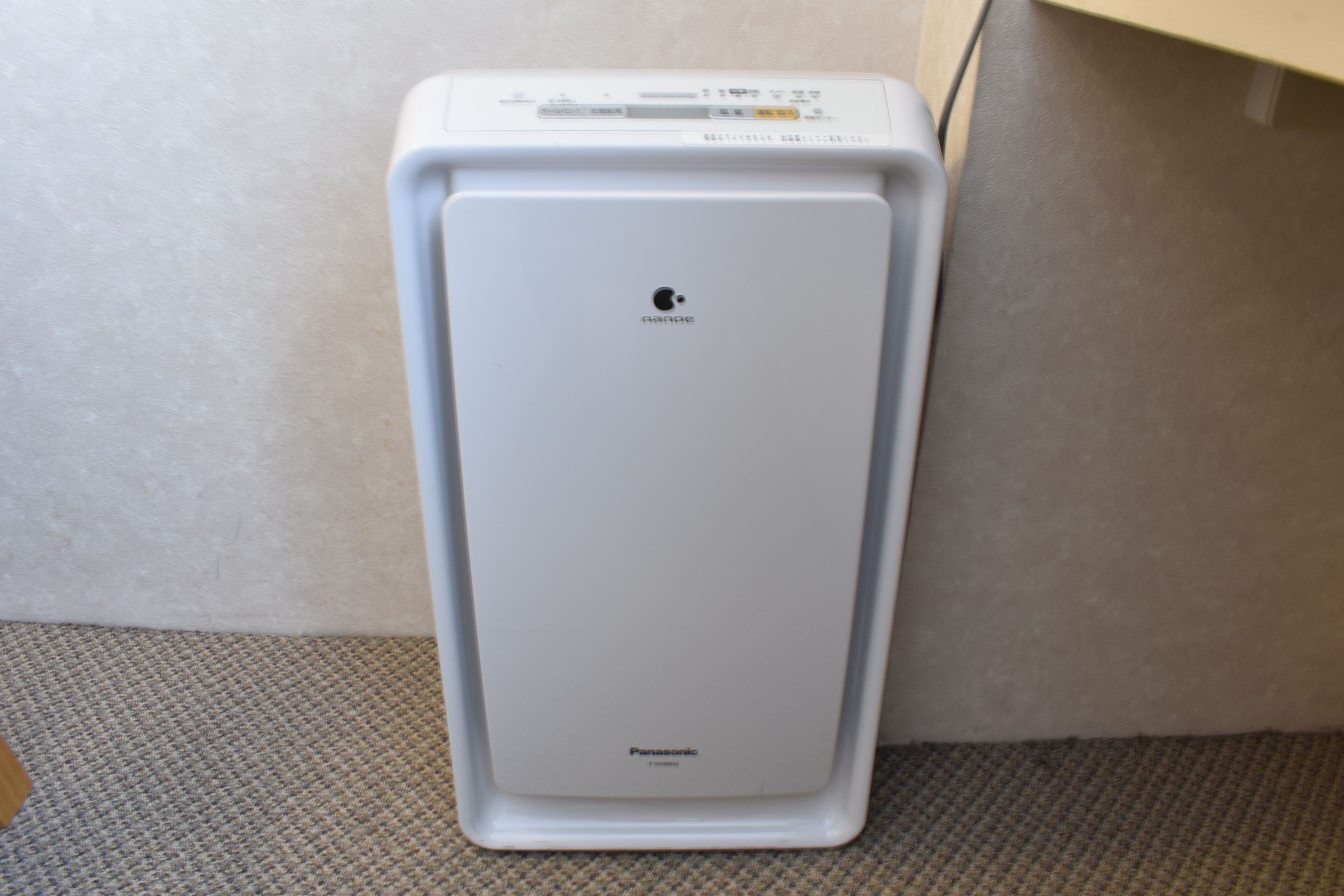 A white Panasonic refrigerator in a corner of a room with a carpeted floor.